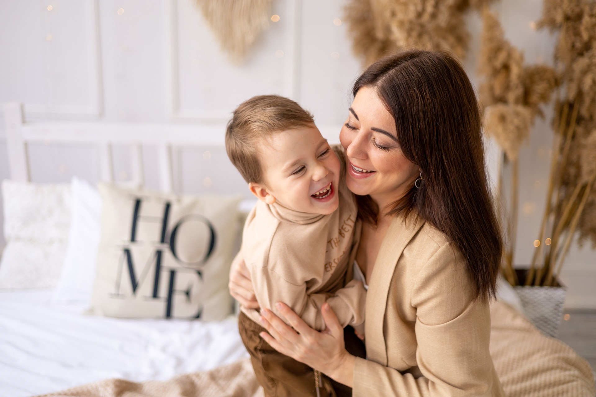 mom and baby boy play, cuddle and fool around at home on a bed in natural brown tones, a happy family with a small child has fun together